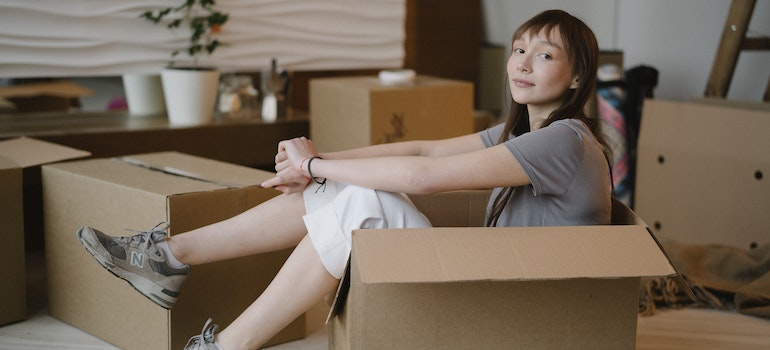 A young woman sitting in a cardboard box waiting for one of the best long distance moving companies to relocate her