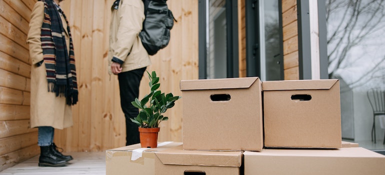 A couple standing on their porch with a bunch of moving boxes in front of them